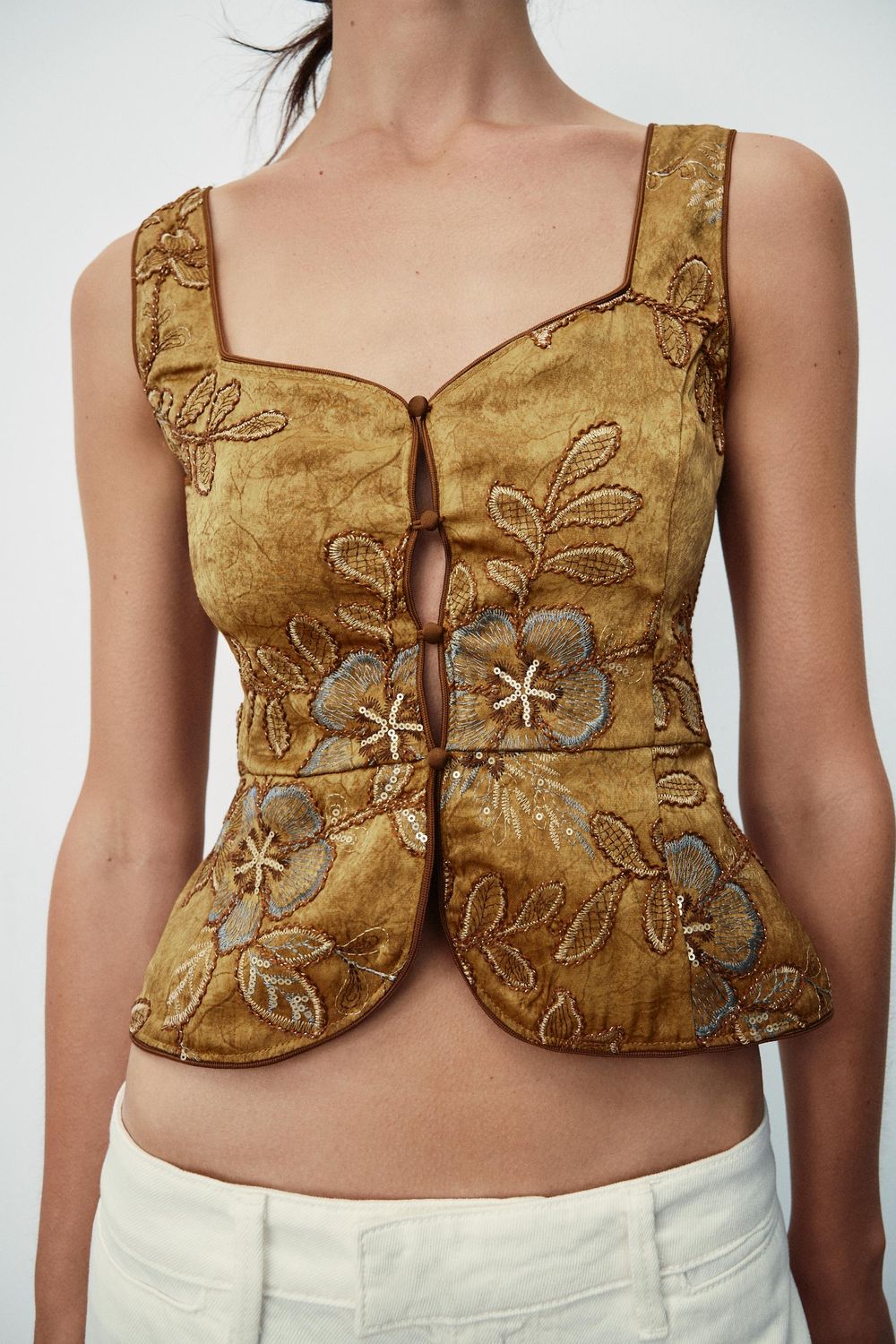 A gold brocade corset top on a model against a plain studio wall.