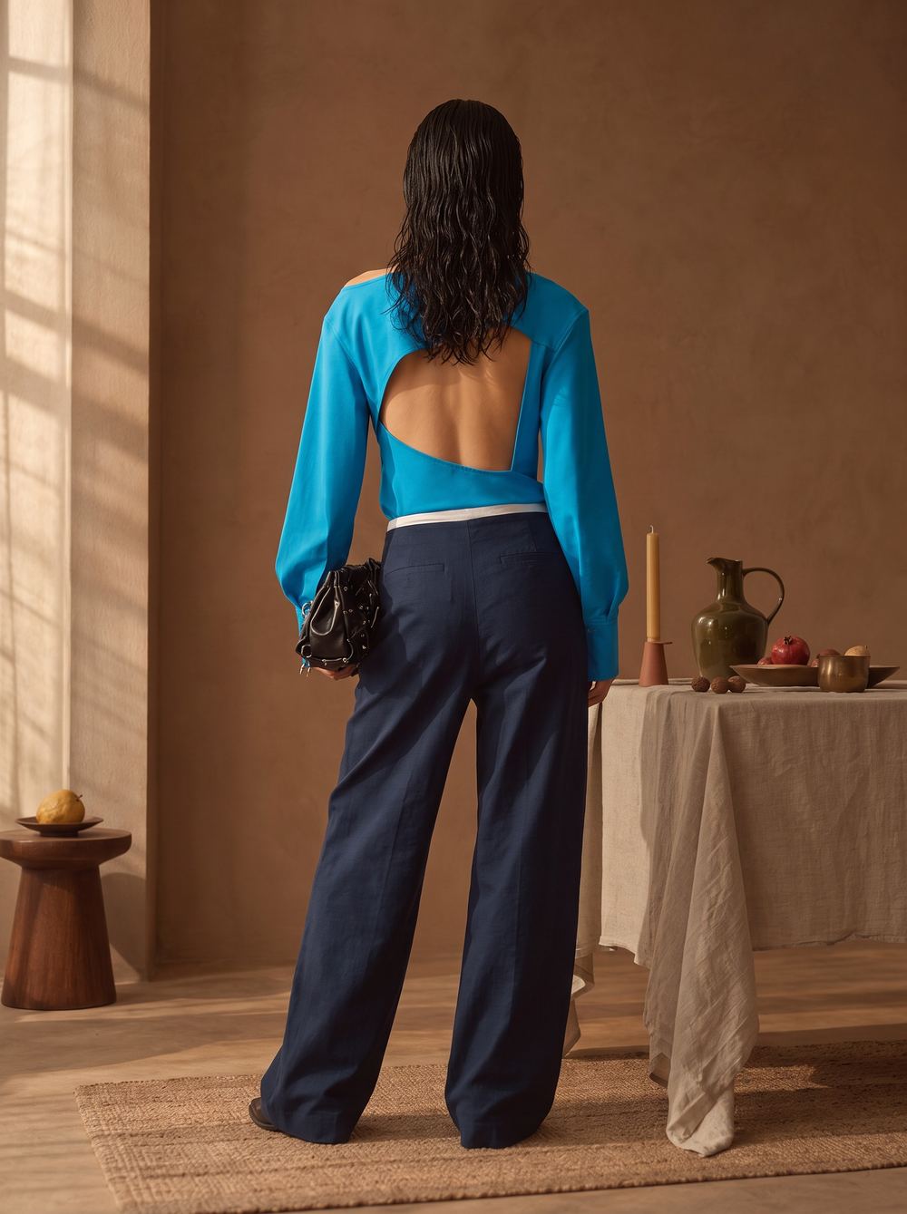 Open-backed blue shirt with navy trousers and a beaded bag.