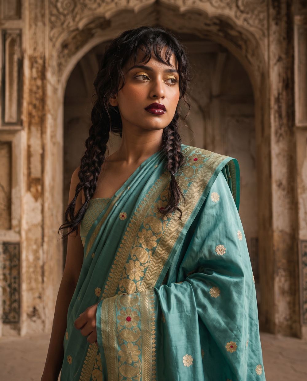 Three-quarter portrait in a teal saree before a carved arch.